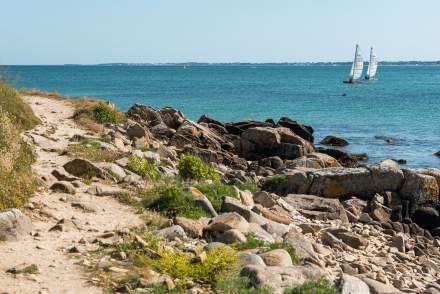 Sentier côtier breton près de Vannes avec rochers, mer turquoise et voilier au large