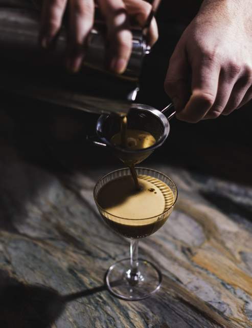Cocktail au Domaine du Liziec dans un verre à pied avec une personne versant un liquide dans une passoire