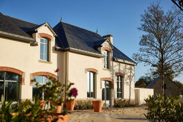 Maison du Domaine du Liziec avec façade beige, toit bleu et jardinières fleuries sous un ciel bleu en journée