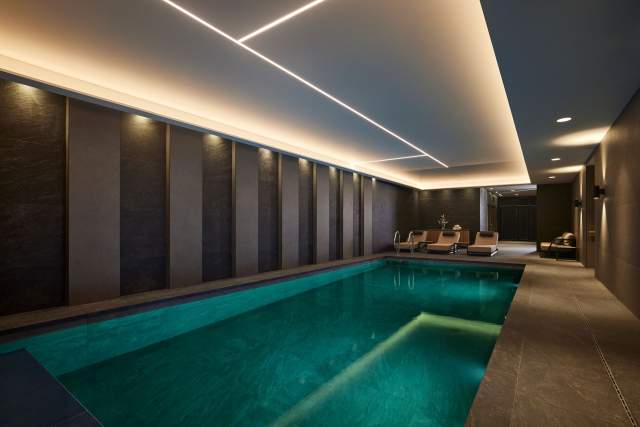 Piscine intérieure du Domaine du Liziec avec eau cristalline, chaises longues et éclairage moderne dans une ambiance luxueuse et sereine