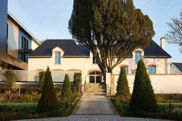 Entrée principale du Domaine du Liziec avec maison symétrique, allée bordée de buissons taillés et jardin paysager soigné