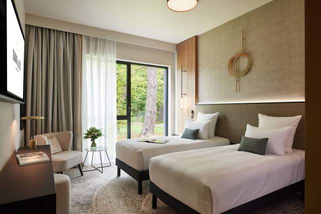 Chambre lumineuse du Domaine du Liziec avec deux lits simples, coin salon fleuri et vue sur la verdure extérieure