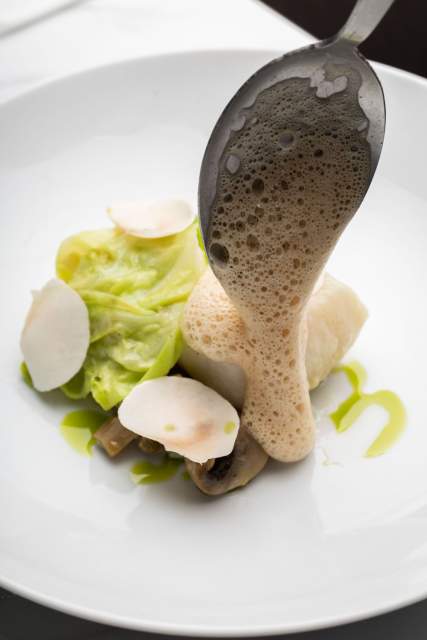 Plat gastronomique au Domaine du Liziec avec filet de poisson ou viande, légumes finement tranchés et sauce mousseuse versée à la cuillère