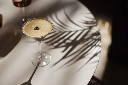 Cocktail raffiné au Domaine du Liziec posé sur une table design avec jeu d’ombres de palmiers