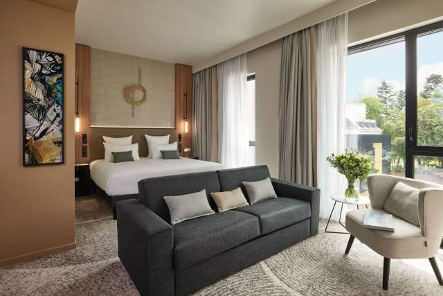 Chambre contemporaine du Domaine du Liziec avec lit double, canapé, lumière naturelle et décoration soignée