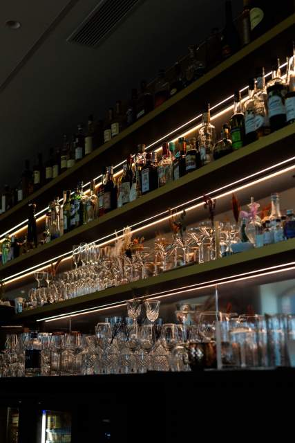 Étagères du bar du Domaine du Liziec avec bouteilles de spiritueux et verrerie, éclairage chaleureux et ambiance raffinée
