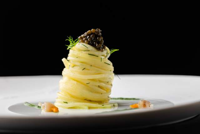Plat gastronomique au Domaine du Liziec, tour de pâtes surmontée de caviar avec herbes fraîches et touche d’agrumes sur assiette blanche