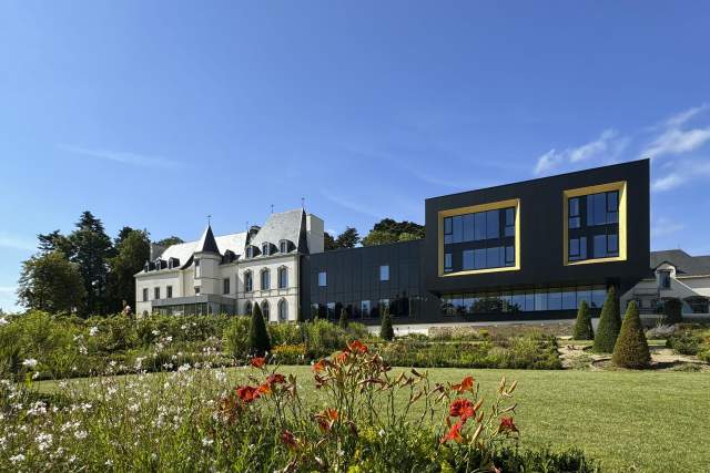 Vue du Domaine du Liziec avec manoir historique et bâtiment moderne, entourés de jardin fleuri sous ciel bleu