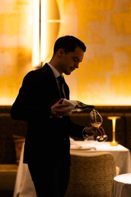 Service de vin au Domaine du Liziec, serveur en tenue élégante versant un grand cru dans une ambiance chaleureuse de restaurant