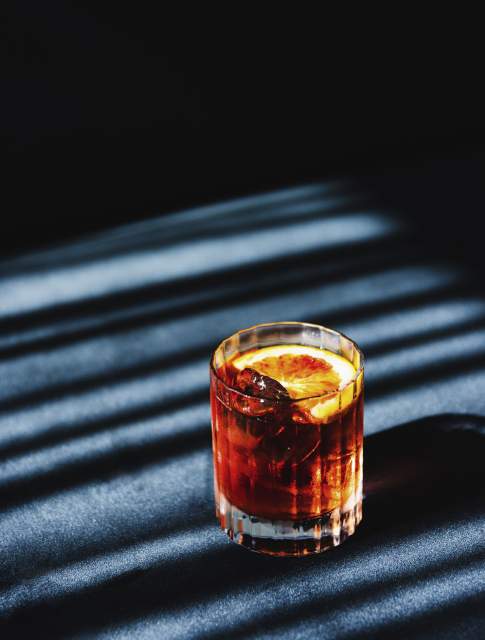 Cocktail au Domaine du Liziec dans un verre à whisky avec tranche d’orange et glaçons, éclairé par des ombres ensoleillées