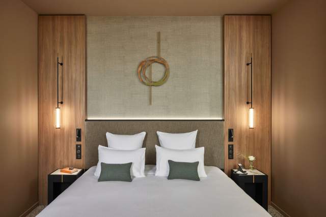 Chambre du Domaine du Liziec avec lit double, coussins verts, décoration murale en bois et éclairage suspendu