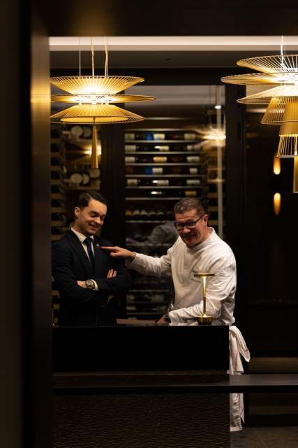 Échange entre chef et invité au Domaine du Liziec dans un cadre chaleureux avec cave à vins et éclairage tamisé