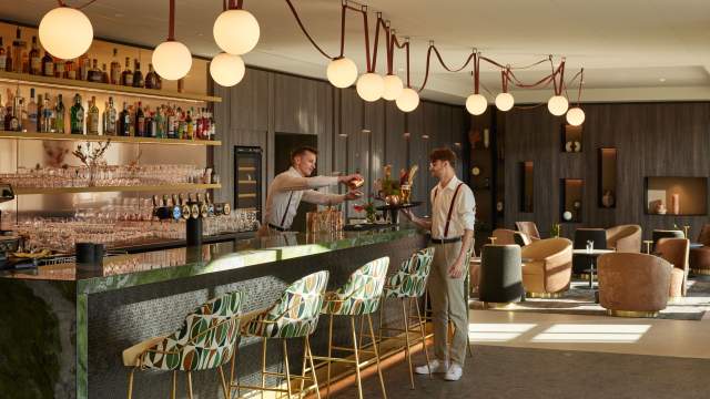 Bar moderne du Domaine du Liziec avec comptoir élégant, éclairage chaleureux, étagères à bouteilles et interaction entre client et barman